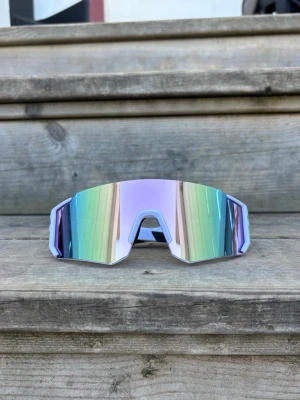 Pastell ljusrosa Sportiga spegelglasade solglasögon - Säljer ett par riktigt snygga sportiga solglasögon med skiftande glas i pastellfärger och bred, kantig form. One size för vuxna. Nya. Unisex. Perfekta för dig som vill sticka ut och få en futuristisk look. Lätta bågar i syntetmaterial och stor lins som täcker bra.