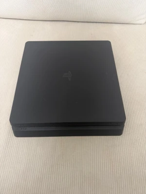 PlayStation 4 Slim spelkonsol svart - Säljer en svart PlayStation 4 Slim från Sony. Konsolen har en stilren, matt finish och den klassiska PlayStation-loggan på ovansidan. Formen är rektangulär med rundade hörn och den har USB-portar framtill för enkel anslutning av handkontroller och tillbehör   ⚠️inga handkontroller ⚠️