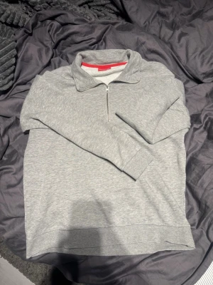 Grå halvzip hoodie från Revolt - Snygg grå halvzip hoodie med hög krage och dragkedja framtill. Tillverkad i mjukt sweatshirtmaterial som är perfekt för chill dagar. Klassisk och enkel design utan tryck eller mönster, passar till det mesta i garderoben.