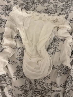 Vit volangtröja med långa ärmar - Säljer en vit tröja med volangdetaljer och långa puffiga ärmar. Tröjan har en offshoulder-design och är gjord i ett tunt, skirt material som ger en romantisk vibe. Perfekt för dig som vill sticka ut med en unik look.