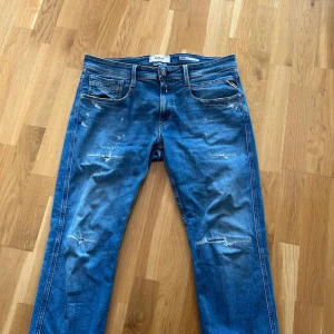 Replay jeans  - Säljer ett par blå jeans från Replay med snygga slitningar och raka ben. Jeansen har klassisk femficksdesign, kontrastsömmar och läderpatch med logga bak i midjan. Änvända fåtal gånger 