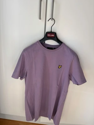 Lyle & Scott: T-Shirt - Säljer en stilren lila t-shirt från Lyle & Scott med klassisk rund hals och korta ärmar. T-shirten har det ikoniska gula fågelmärket broderat på bröstet. Tillverkad i mjuk bomull som känns skön mot huden. Perfekt till jeans eller shorts och en stilren sommarlook! 🎉T-Shirten är köpt på Lyle&Scott’s outletbutik i Barkarby och har aldrig använts därav väldigt bra pris! 🎉För mer info skriv på dm!