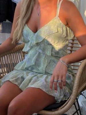 Ljusgrön volangklänning med prickar - Söt ljusgrön kortklänning med vita prickar och volangdetaljer. Klänningen har v-ringning, tunna axelband och är tillverkad i ett lätt, luftigt material som passar perfekt till varma dagar. Stilren och trendig design som ger en romantisk känsla. använd en gång 