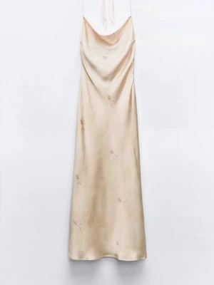 Champagnefärgad långklänning i satin - Säljer en elegant långklänning i champagnefärgad satin med tunna axelband och diskret broderade blommor. Klänningen har en mjuk, draperad urringning och öppen rygg. Perfekt för sommarens alla tillfällen! Endast använd ett fåtal gånger.