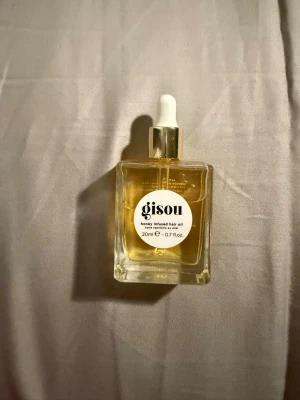 Gisou Honey Infused Hair Oil 20ml - Gisou Honey Infused Hair Oil i en genomskinlig fyrkantig glasflaska med pipett och guldfärgat lock. Innehåller 20 ml närande hårolja med honungsextrakt som ger glans och mjukhet till håret. Perfekt för att boosta hårets fukt och lyster.