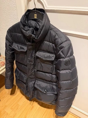 Mörkgrå pufferjacka från Moncler - Snygg mörkgrå pufferjacka från Moncler med hög krage och fyra fickor. Säljs nu för endas 2399. Storlek 1, passar S/M hör av er vid frågor 