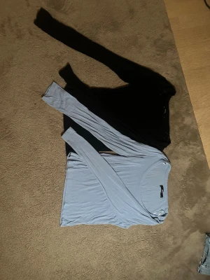 Två långärmade toppar i svart och ljusblå - Säljer två stilrena långärmade toppar, en i svart och en i ljusblå. Båda har rund halsringning och är tillverkade i ett mjukt, stretchigt material som sitter skönt på kroppen. Perfekta att matcha med jeans eller kjol för en enkel och snygg look.