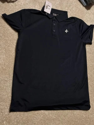 Marinblå pikéskjorta Cross Sportswear - Snygg marinblå pikéskjorta från Cross Sportswear i klassisk modell. Skjortan har krage, knappar framtill och är tillverkad i ett mjukt bomullsmaterial som känns skönt mot huden. Perfekt för dig som gillar stilrena och sportiga plagg.