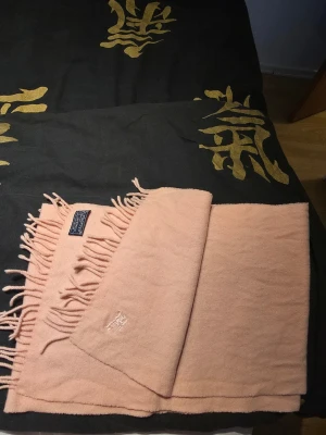 Vintage Ljusrosa halsduk från Burberry - Supersnygg ljusrosa halsduk från Burberry i mjuk ull. Halsduken har klassiska fransar i kanterna och en diskret broderad Burberry-logga. Perfekt accessoar för att lyfta din outfit med en touch av lyx.