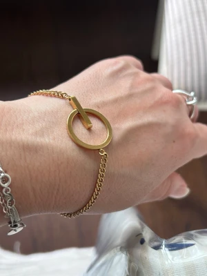 Edblad armband - Snyggt armband i Guldplaterad stål metall med en öppen cirkel och stång som detalj framtill. Kedjan är tunn och elegant, vilket ger en minimalistisk och modern look. Perfekt för dig som gillar stilrena accessoarer.