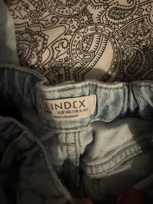 Ljusblå raka jeans från Lindex - Säljer ett par ljusblå jeans från Lindex i rak modell. Jeansen har klassisk femficksdesign, resår i midjan och råa kanter vid bensluten för en avslappnad look. Perfekta till en chill outfit och lätta att matcha med olika stilar.