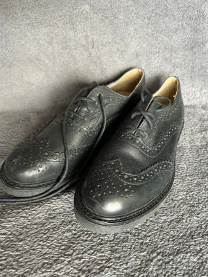 Black Leather Brogue Oxford Shoes – Classic Style - Klassiska brogue / oxford-skor i svart läder med dekorativa perforerade detaljer.  En tidlös modell som passar perfekt till kostym, business eller klassisk stil.  Detaljer • XIT • Svart läder • Brogue / Oxford design • Snörning • Elegant klassisk modell  Perfekta till kostym, chinos eller mer dressade outfits.  📦 Skickas snabbt 💬 Hör gärna av dig vid frågor