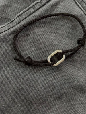Svart snörearmband med metallspänne - Stilrent armband med svart justerbart snöre och ett silverfärgat metallspänne i form av en karbinhake. Perfekt för dig som gillar minimalistiska accessoarer med en sportig touch.