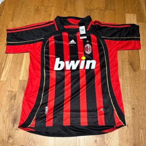 AC Milan home kit 06/07 Pirlo #21 - Säljer en klassisk AC Milan matchtröja från Adidas med Pirlo 21 på ryggen. Tröjan har röda och svarta vertikala ränder, klubbmärke på bröstet och Bwin som sponsor. Tillverkad i lätt polyester, perfekt för fotboll eller samling.