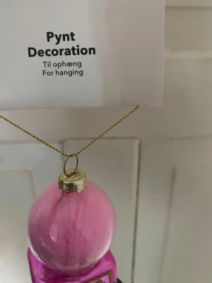 Julgranspynt sockervaddsvagn rosa - Hängande dekoration i form av en sockervaddsvagn i glas, målad i olika rosa nyanser med gulddetaljer och svart hjul. Perfekt som unik julgransprydnad eller dekoration till högtider. Kommer med guldfärgad upphängningstråd.