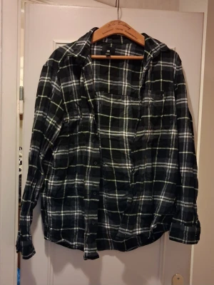 2 st Rutiga skjortor från H&M - Snygg svart skjorta från H&M med vitt och grönt rutmönster. Skjortan har långa ärmar, klassisk krage och knäppning framtill. Perfekt för en avslappnad och trendig stil. Båda skjortorna för 250 kr