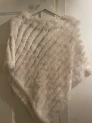 Vit fluffig pälsväst - Supermjuk och lyxig ljusbeige pälsväst med breda diagonala ränder. Västen har en klassisk, rak passform och är tillverkad i fuskpäls som känns riktigt mjuk. Perfekt för att addera en trendig touch till din outfit.