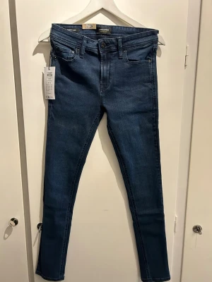 Mörkblå skinny/Liam  jeans från Jack&Jones - Snygga mörkblå skinny jeans från Only med klassisk femficksdesign och normalhög midja. Jeansen har stretchigt material för skön passform och smala ben. Perfekta till en avslappnad eller trendig look.
