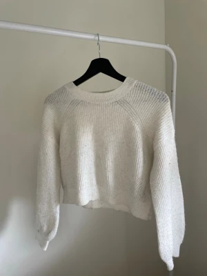 Vit cropped stickad tröja - (Har en fläck på ena armen som jag visar på sista bilden) Säljer en vit, cropped stickad tröja med breda ärmar och ribbade muddar. Tröjan har en avslappnad passform och rund halsringning. Perfekt för lager på lager och enkel att styla till olika outfits.