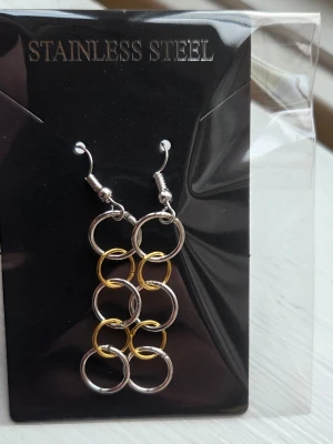 Örhängen i rostfritt stål, silver/guld - Snygga örhängen i rostfritt stål med en modern design av sammanlänkade ringar i både silver- och guldfärg. Hängande modell som ger en cool och trendig look. Perfekta för dig som gillar stilrena accessoarer med en twist.
