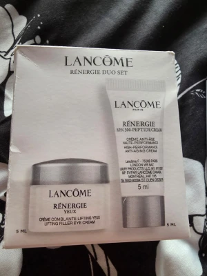 Lancôme Rénergie Duo Set 5ml - Lancôme Rénergie Duo Set innehåller två produkter: en ögonkräm (Rénergie Yeux) och en ansiktskräm (H.P.N. 300-Peptide Cream), båda i 5 ml förpackningar. Setet kommer i en vit och silverfärgad kartong och är perfekt för dig som vill testa anti-age hudvård från Lancôme.