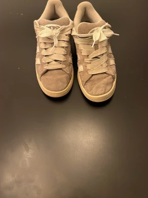 Beige Adidas campus sneakers i mocka - Säljer ett par beige Adidas campus sneakers i mocka med klassiska vita ränder på sidan. Skorna har vita snören och en beige sula. Låg modell som passar perfekt till jeans eller shorts. Riktigt sköna.