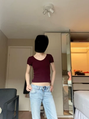 Mörkröd croppad topp - En enkel och stilren mörkröd croppad topp med korta ärmar och rund eller lite triangel aktig  halsringning. Perfekt att matcha med jeans eller kjol för en avslappnad look. Toppens passform är tight och den har en slät yta utan mönster eller detaljer.