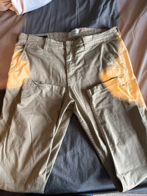 Beige cargobyxor från Jack & Jones - Snygga beige cargobyxor från Jack & Jones med klassiska stora sidofickor och raka ben. Tillverkade i ett mjukt bomullstyg som är bekvämt att bära. Perfekta för en avslappnad och trendig stil.
