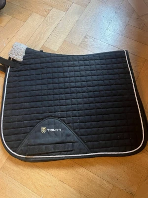 Svart schabrak från Trinity!!! - Säljer ett svart schabrak från Trinity med vit kant. Storlek pony och  använts till min c ponny, funkar perfekt på henne även fast hon var lite rund!! 