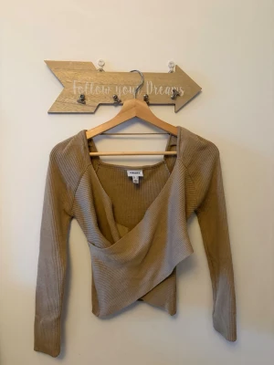 Beige omlottopp från AWARE/ Nelly  - Trendig beige omlottopp från AWARE köpt från Nelly med ribbad struktur och lång ärm. Toppen har en snygg omlottdesign framtill och är lite croppad i modellen. Perfekt för dig som gillar stilrena och moderna plagg. Ärmarna har jag också sytt in lätt som man även lätt kan ta ut om man önskar att ha de längre.