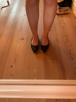 Svarta ballerinaskor med spetsig tå - Säljer ett par stilrena svarta ballerinaskor med spetsig tå och låg klack. Skorna har en klassisk design och är tillverkade i ett slätt material som ger en elegant look. Perfekta för dig som vill ha en enkel och snygg sko till din outfit. Endast använda en gång. 