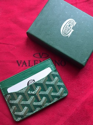 Grön korthållare  - Snygg grön korthållare från vet ej med det klassiska mönstret i vitt och brunt. Tillverkad i tåligt läder med plats för flera kort. Perfekt accessoar för dig som vill ha något stilrent och exklusivt i fickan.