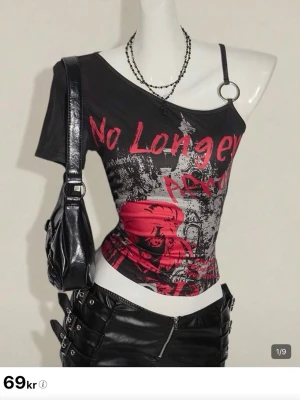 Shein tröja med tryck - Säljer en svart asymmetrisk topp med grafiskt tryck i rött och grått. Toppen har en unik design med en axelbandslös sida och en metallring på axelbandet. Tight passform och croppad längd, perfekt för en edgy stil. Varan har aldrig blivit använd förutom för provtagning 🤍