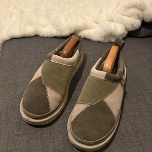  UGG herr - Snygga och bekväma utomhus tofflor från UGG i olivgrönt och beige. Skorna har en robust sula och är perfekta för en avslappnad stil. De har en unik design med olika färgblock och är lätta att ta på och av. 