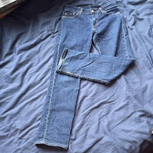 Blå raka jeans från Levi's - Klassiska blå jeans från Levi's med raka ben och fem fickor. Jeansen har en traditionell knappgylf och synliga sömmar. Tillverkade i slitstark denim med en tidlös passform och ikonisk läderpatch bak i midjan.