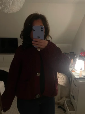 Vinröd chunky kofta med stora knappar - Mysig vinröd stickad kofta med oversized passform och stora silvriga knappar framtill. Koftan har två fickor och långa ärmar, perfekt för lager-på-lager-stil. Passar dig som gillar en avslappnad och trendig look.