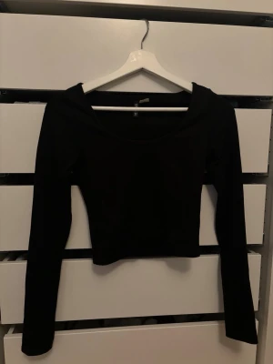 Svart ribbad crop top - Säljer en svart ribbad crop top från H&M med långa ärmar och rundad urringning. Toppen är tight i modellen.