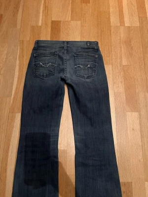 Mörkblå bootcut jeans  - Snygga mörkblå bootcut jeans från 7 for all mankind, med klassisk femficksdesign och broderade detaljer på bakfickorna. Jeansen har låg midja och är tillverkade i ett mjukt denimtyg med lätt tvättad look. Perfekta för en avslappnad och trendig stil. Jeansen är stretchiga och anpassar sig i storleken. 