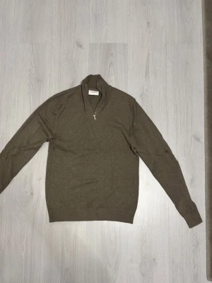 Brun halvzip-tröja från Lindberg - Snygg brun långärmad tröja från Lindberg  med halv dragkedja vid halsen. Tröjan har ribbade muddar vid ärmslut och nederkant, samt en klassisk passform. Perfekt för lager-på-lager och stilrena outfits.