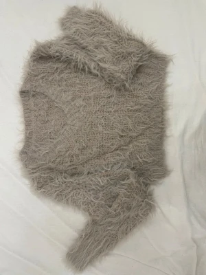 Beige fluffig stickad tröja - Supermjuk och fluffig stickad tröja i beige med lång ärm och v-ringning. Tröjan har en lurvig textur som ger en mysig och trendig look. Perfekt för dig som gillar att sticka ut med en unik och cozy stil.