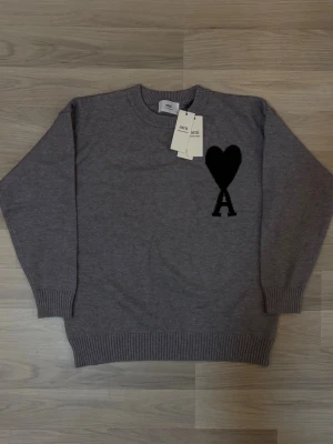 Grå stickad tröja från Ami Paris ~ S - Säljer en grå stickad tröja från Ami Paris med svart hjärta och bokstaven A broderat på bröstet. Fraktar samma dag, ställ frågor privat👌🏽