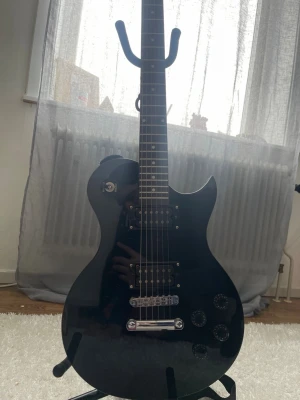 Svart elgitarr Gear4music - Säljer en svart elgitarr från Gear4music med klassisk Les Paul-inspirerad form. Gitarren har två humbucker-mickar, tre kontrollrattar och kromad stämskruv. Perfekt för dig som vill börja spela elgitarr eller behöver ett extra instrument till replokalen. Sparsamt använd. Inköptes nytt. Fungerar felfritt. Säljs med stand 