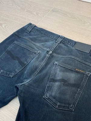 Svarta Nudie Jeans - Säljer ett par svarta jeans från Nudie Jeans med klassisk femficksmodell och snygga slitningar. Jeansen har Nudie Jeans karaktäristiska brodyr på bakfickorna och svart läderpatch i midjan. Tillverkade i slitstark denim med cool tvätt. Hör av dig vid minsta lilla fråga🙏😊