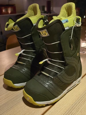 Burton snowboardboots olivgrön/gul - Snowboardboots från Burton i olivgrönt med gula detaljer och vit sula. Bootsens modell heter Emerald och har snabbsnörning samt vadderad insida för extra komfort. Perfekta för dig som vill ha stilrena och funktionella boots i backen. Storlek 37 med Innermått 23,3 cm.