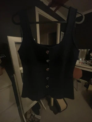 Helt ny topp med knappar - Snygg marin blå topp med breda axelband och dekorativa knappar framtill. Toppen har en figurnära passform och är perfekt att styla med jeans eller kjol. Materialet känns mjukt och stretchigt. storlek M skulle säga true to size men stretchiga så kan passa lite större 