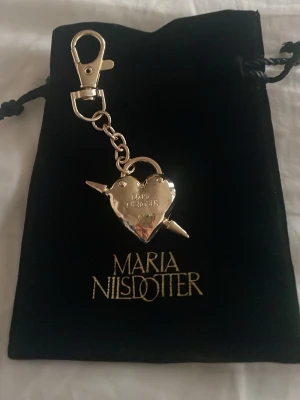 Nyckelring hjärta Maria Nilsdotter - Säljer en snygghet ny  nyckelring från Maria Nilsdotter i guld hjärtformad berlock. Nyckelringen är guld och kommer i en svart sammetsförvaringspåse från marianillsdotter.med guldfärgad logga. Perfekt accessoar till väskan eller nycklarna.❤️✨