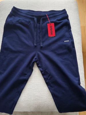 Mörkblå mjukisbyxor från HUGO - Snygga mörkblå mjukisbyxor från HUGO med dragsko i midjan och ribbade muddar vid bensluten. Byxorna har diskret HUGO-logga på vänster sida och är tillverkade i mjukt bomullsmaterial för maximal komfort.