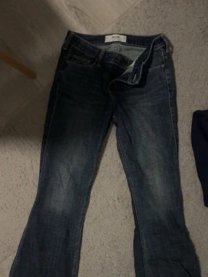 Blå low-rise flare jeans Hollister - Säljer ett par blå low-rise flare jeans från Hollister. Jeansen har klassisk femficksdesign, låg midja och utsvängda ben. Tillverkade i denim med snygga slitningar och tvättade detaljer för en avslappnad look.