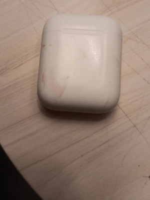 Apple AirPods - Säljer ett par vita Apple AirPods.Hörlurarna har en stilren och kompakt design i plast, perfekt för trådlös musik och samtal. Etuiet är smidigt att ta med sig och laddar hörlurarna automatiskt när de ligger i. Har en färg på som är svår att få bort men funkar