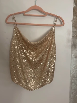 Glittrig guld paljettopp med tunna band - Snygg glittrig topp i guld med tunna axelband och draperad front. Hela toppen är täckt av paljetter som ger ett riktigt festligt intryck💕